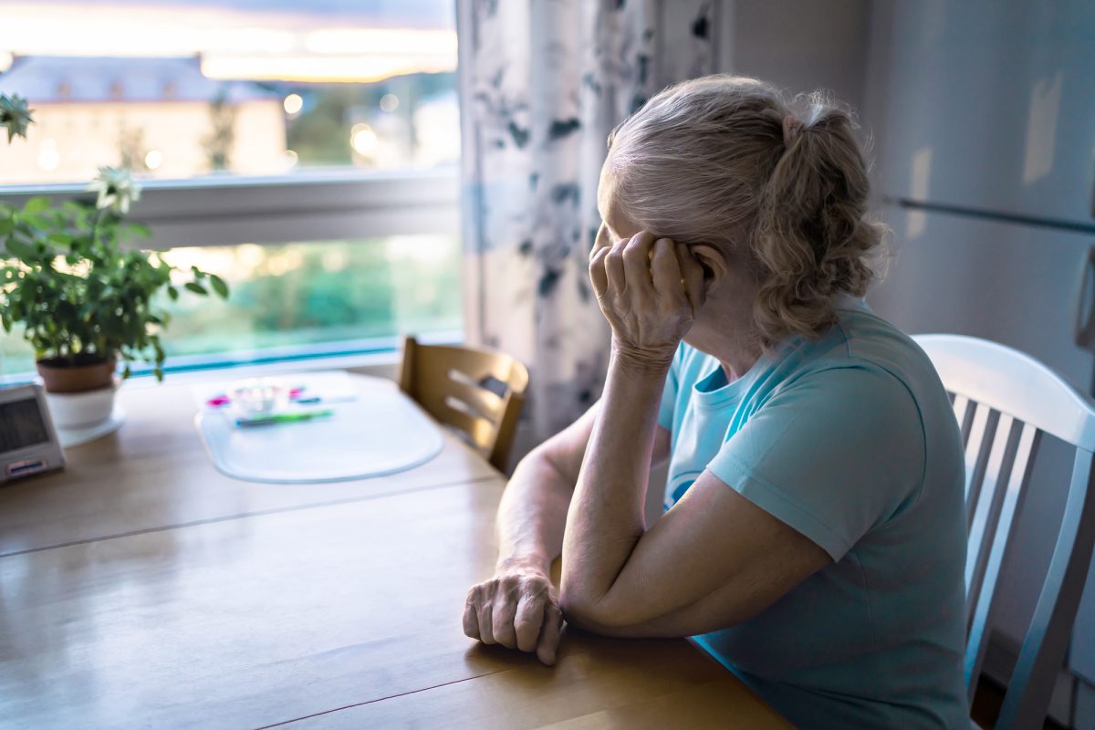 Seniori-ikäinen nainen yksin kotona ikkunan ääressä.