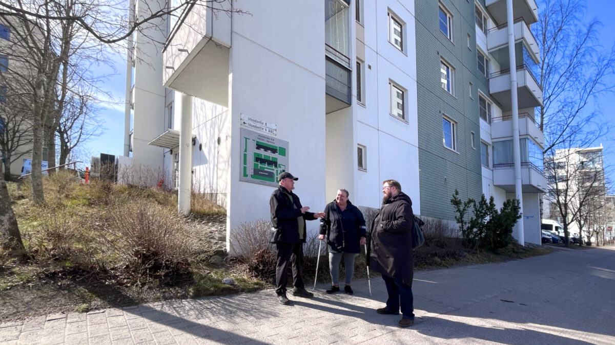 kolme henkilöä keskustelee talon edustalla